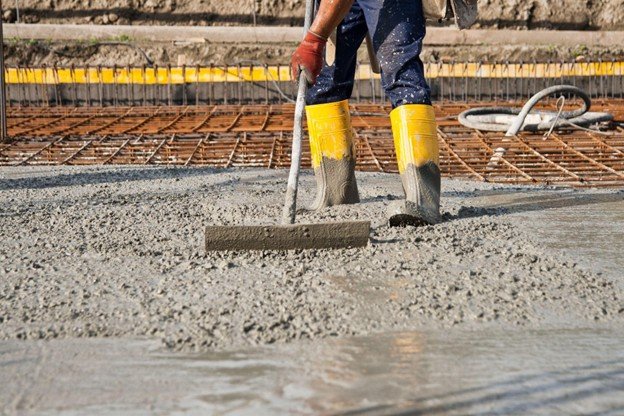 Construction worker leveling freshly poured concrete slab over steel rebar during foundation installation at a building site