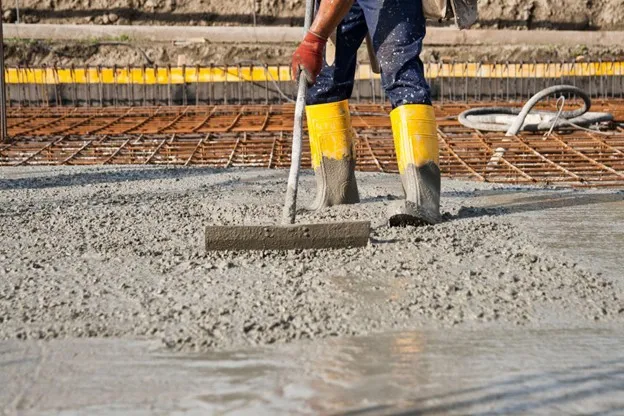Construction worker leveling freshly poured concrete slab over steel rebar during foundation installation at a building site